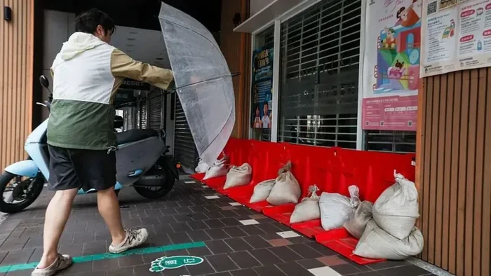 seorang-pejalan-kaki-membawa-payung-saat-melintas-di-dekat-karung-pasir-dan-penghalang-banjir-yang-dipasang-di-depan-sebuah-ba-1792737932883_169